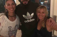 Three people are standing together indoors, smiling at the camera. The person in the middle is wearing a black Adidas hoodie. Three people are standing together indoors, smiling at the camera. The person in the middle is wearing a black Adidas hoodie.