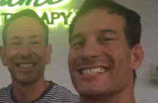 Two smiling men are taking a selfie in front of a neon sign that reads "Miami Therapy." One wears a striped shirt and the other a black shirt. Two smiling men are taking a selfie in front of a neon sign that reads "Miami Therapy." One wears a striped shirt and the other a black shirt.