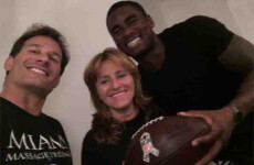 Three people are smiling at the camera; one is holding a football. The person on the left is wearing a shirt with the text "MIAMI MASSAGE THERAPY. Three people are smiling at the camera; one is holding a football. The person on the left is wearing a shirt with the text "MIAMI MASSAGE THERAPY.