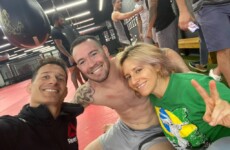 Three people are smiling for a photo in a gym. One person is shirtless, seated in the middle, while the other two are on either side, one wearing a Reebok jacket and the other in a green shirt doing a peace sign. Three people are smiling for a photo in a gym. One person is shirtless, seated in the middle, while the other two are on either side, one wearing a Reebok jacket and the other in a green shirt doing a peace sign.