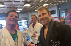 Three people in martial arts uniforms smiling in a gym, with a boxing ring in the background. Three people in martial arts uniforms smiling in a gym, with a boxing ring in the background.
